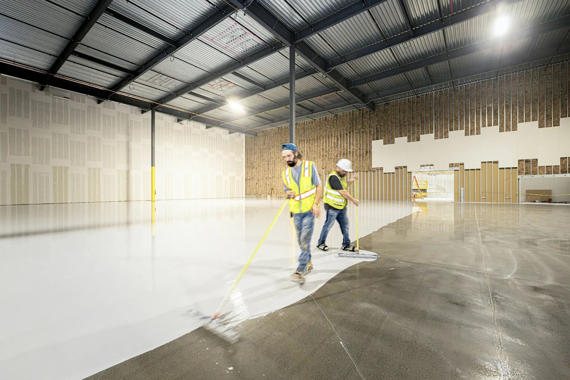 Crew rolling a coating across a large commercial warehouse floor